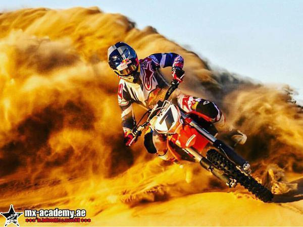 Desert ride Dubai: a rider on a red motocross bike carves through a dune and throws up a huge wave of golden sand