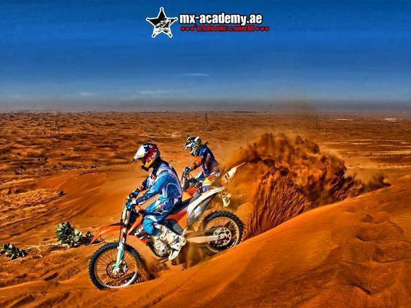 Dirt bike Dubai in the dunes: two riders cut down a sandy slope, a fountain of sand behind the rear bike