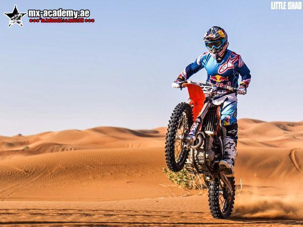 Dirt bike Dubai video: rider lifting the front wheel of his bike in front of sand dunes