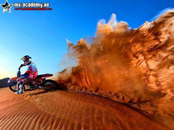Dirt bike in Dubai: a rider turns on a sand dune and throws a huge plume of orange sand into the blue sky