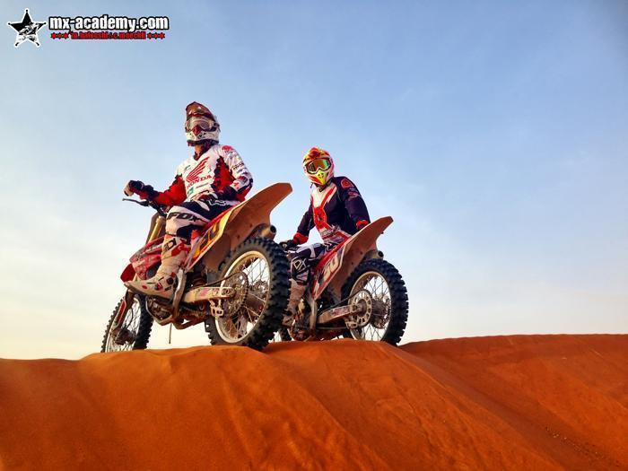Dirt biking in Dubai: a rider in a white Honda jersey and one with a yellow helmet pause side by side on a dune