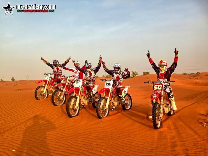 Dubai motocross: five riders on red bikes raise their arms in the rippled red sand of the desert