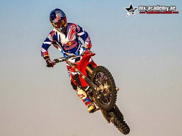 Enduro riding in Dubai: a rider in Red Bull kit jumps a red bike high against a pale, hazy sky