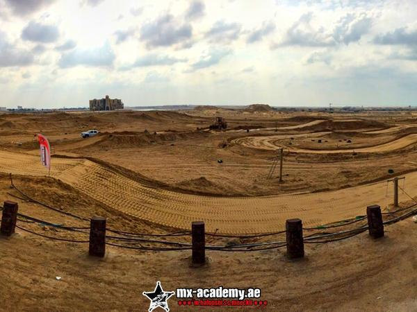 How to find the MX-Academy in Dubai: wide view of a sandy track behind wooden posts and ropes, buildings on the horizon