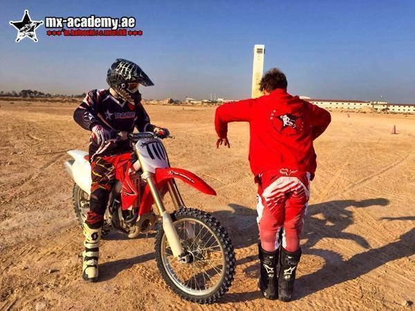 Motocross for kids in Dubai: coach in a red hoodie shows a young rider on a red Honda the right body position