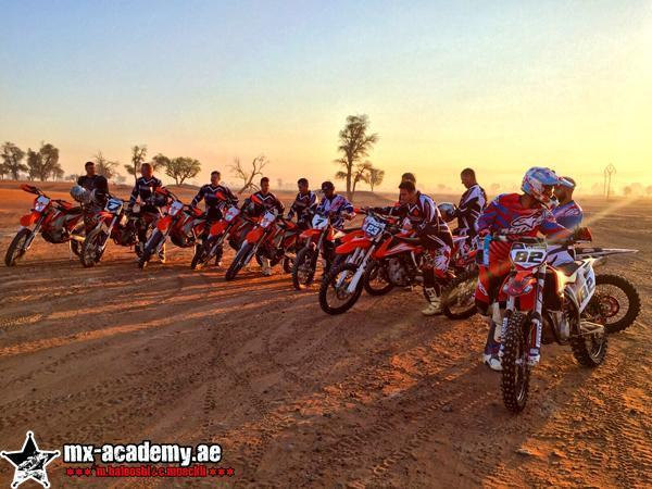 Motorcycle desert safari Dubai: a row of riders with orange and red bikes lines up on the sand in low golden light